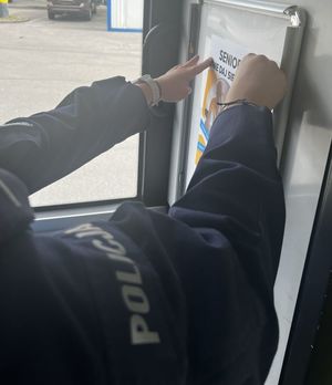 Zdjęcie przedstawiające ręce policjantki, która zamieszcza plakat w autobusie