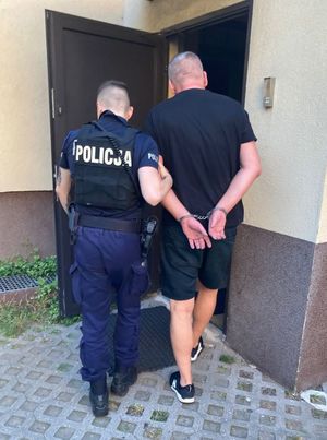 Zdjęcie przedstawiające policjanta, prowadzącego zatrzymanego mężczyznę