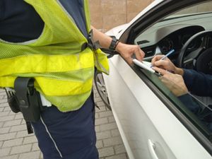 Zdjęcie przedstawiające policjanta podczas wręczania kierującemu do podpisu bloczka mandatowego