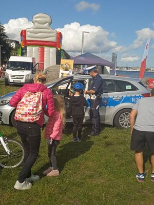 Zdjęcie przedstawiające policjanta, kobietę i dwójkę dzieci na tle radiowozu