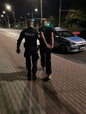 Zdjęcie przedstawiające policjanta, prowadzącego zatrzymanego mężczyznę