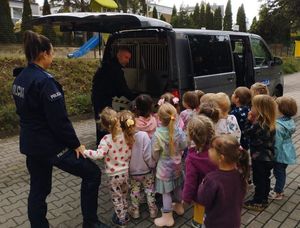 Zdjęcie przedstawiające policjantkę i policjanta oraz dzieci na tle radiowozu