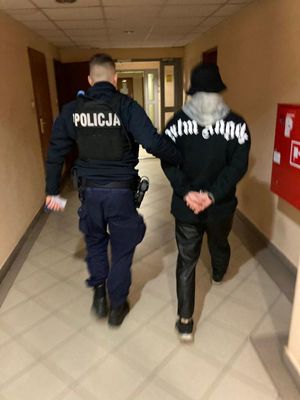 Zdjęcie przedstawiające policjanta prowadzącego zatrzymanego mężczyznę