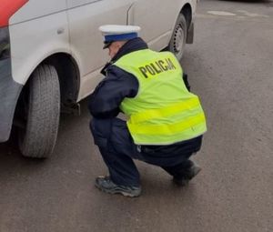 Zdjęcie przedstawiające policjanta, sprawdzającego opony w pojeździe