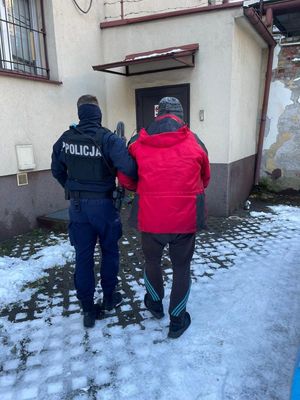 Zdjęcie przedstawiające policjanta prowadzącego zatrzymanego mężczyznę