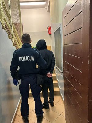 Zdjęcie przedstawiające policjanta prowadzącego zatrzymanego mężczyznę