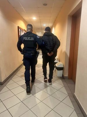 Zdjęcie przedstawiające policjanta, który prowadzi zatrzymanego mężczyznę