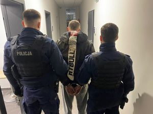 Zdjęcie przedstawiające dwóch policjantów prowadzących zatrzymanego mężczyznę