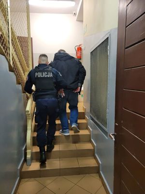 Zdjęcie przedstawiające policjanta, który prowadzi zatrzymanego mężczyznę