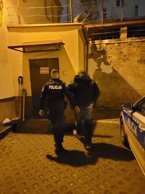 Zdjęcie przedstawiające policjanta, który prowadzi zatrzymanego mężczyznę