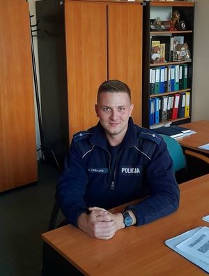 Zdjęcie przedstawiające policjanta, który siedzi w biurze przy stole