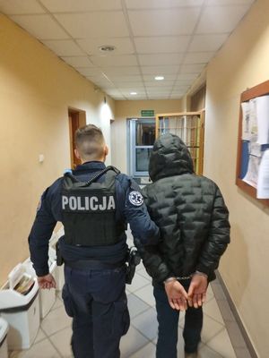 Zdjęcie przedstawiające policjanta, który prowadzi zatrzymanego mężczyznę