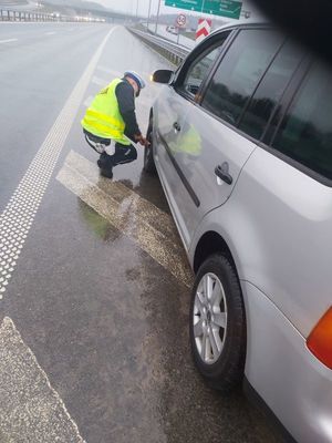 Zdjęcie przedstawiające policjanta ruchu drogowego, który wymienia obywatelowi koło w samochodzie