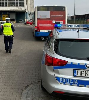 Zdjęcie przedstawiające policjanta podczas kontroli autobusu miejskiego. Na zdjęciu widać radiowóz policyjny, autobus i w tle samochód osobowy.