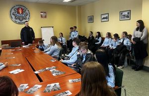 Zdjęcie przedstawiające uczniów ze szkoły średniej, którzy są w sali odpraw i rozmawiają z Komendantem Miejskim Policji w Gdyni. Na zdjęciu widać również nauczycielkę.