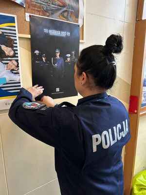 Zdjęcie przedstawiające policjantkę, zamieszczającą na tablicy ogłoszeń plakat dotyczący doboru do Policji