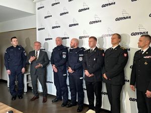 Zdjęcie przedstawiające od lewej Komendanta Miejskiego Policji w Gdyni, Prezydenta Miasta Gdyni, dwóch policjantów, dwóch funkcjonariuszy Państwowej Straży Pożarnej oraz Komendanta Miejskiego Państwowej Straży Pożarnej w Gdyni