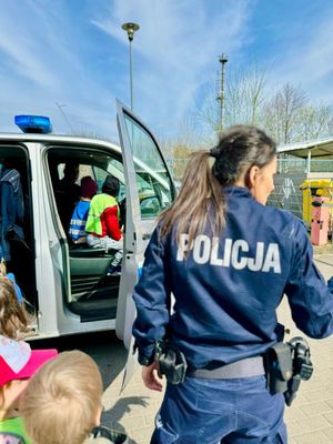 Zdjęcie przedstawiające policjantkę, która stoi przed radiowozem policyjnym, w którym siedzą dzieci.