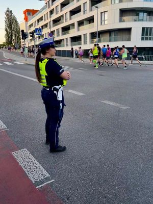 Zdjęcie przedstawiające policjantkę ruchu drogowego, która zabezpiecza bieg. W tle widać uczestników biegu.