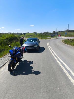 Zdjęcie przedstawiające motocykl oraz nieoznakowany radiowóz, przy którym stoi mężczyzna.