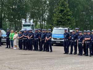 Zdjęcie przedstawiające stojących na placu, na tle radiowozów policjantów ruchu drogowego oraz dwie kobiety