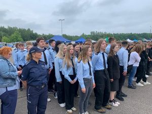 Zdjęcie przedstawiające policjantkę oraz uczniów klas o profilu policyjnym. Wszyscy stoją na placu.