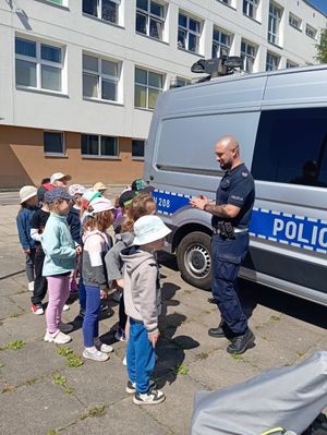 Zdjęcie przedstawiające policjanta, który rozmawia z dziećmi na temat bezpieczeństwa w ruchu drogowym.