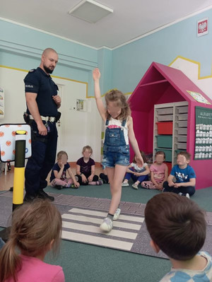 Zdjęcie przedstawiające policjanta, który rozmawia z dziećmi na temat bezpieczeństwa w ruchu drogowym.