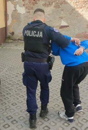 Zdjęcie przedstawiające policjanta prowadzącego zatrzymanego mężczyznę