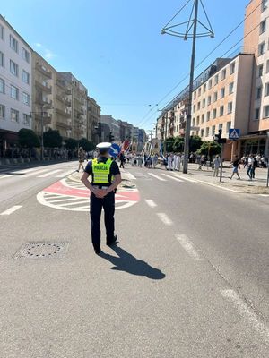 Zdjęcie przedstawiające policjanta, który stoi na ulicy i zabezpiecza procesję