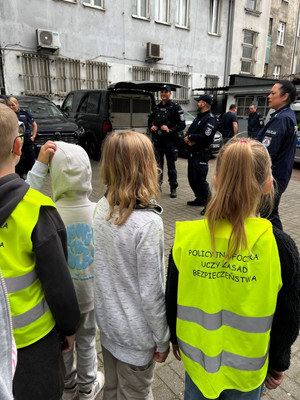 Zdjęcie przedstawiające policjantów na tle radiowozu policyjnego. Mundurowi stoją przodem do uczniów.