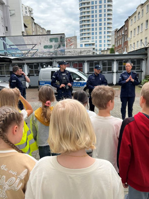 Zdjęcie przedstawiające policjantów na tle radiowozu policyjnego. Mundurowi stoją przodem do uczniów.