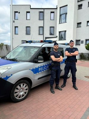 Zdjęcie przedstawiające dwóch policjantów na tle radiowozu, którzy uratowali kobietę