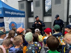 Zdjęcie przedstawiające dwóch policjantów, reprezentujących dzieciom stojącym na przeciwko broń służbową