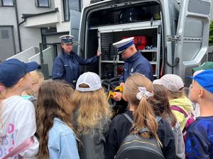 Zdjęcie przedstawiające policjantkę i policjanta z ruchu drogowego, którzy pokazują dzieciom wyposażenie radiowozu.