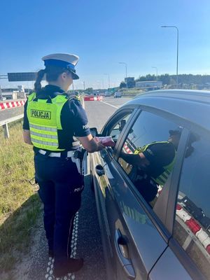 Zdjęcie przedstawiające policjantkę, wręczającą kierowcy apteczkę samochodową