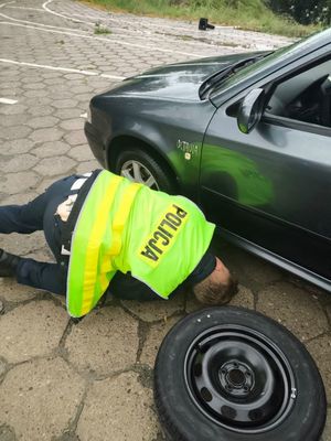 Zdjęcie przedstawiające policjanta, który wymienia koło w samochodzie.