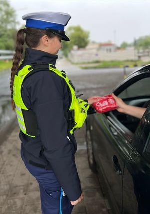 Zdjęcie przedstawiające policjantkę ruchu drogowego, która wręcza kierowcy apteczkę samochodową