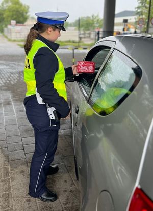 Zdjęcie przedstawiające policjantkę ruchu drogowego, która wręcza kierowcy apteczkę samochodową