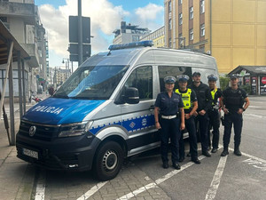 Zdjęcie przedstawiające policjantów na tle oznakowanego radiowozu.