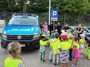 Zdjęcie przedstawiające policjantki, policjantów, przedszkolaków i ich opiekunkę. Wszyscy stoją na placu przy radiowozie policyjnym.