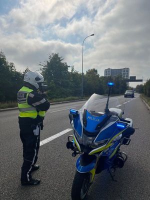 Zdjęcie przedstawiające policjanta stojącego przy motocyklu i wykonującego pomiar prędkości.