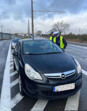 Zdjęcie przedstawiające policjantów podczas kontroli drogowej. Na zdjęciu widać samochód osobowy oraz stojący za nim radiowóz policyjny.