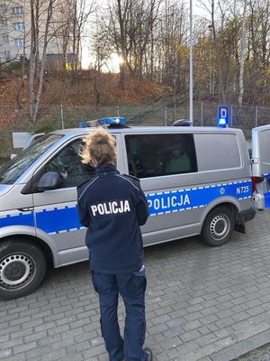Zdjęcie przedstawiające policjantkę stojącą tyłem na tle radiowozu