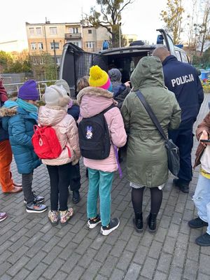 Zdjęcie przedstawiające policjanta i dzieci stojących tyłem przy radiowozie
