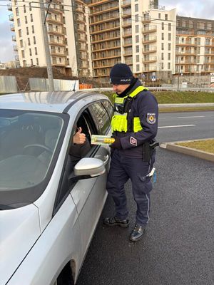 Zdjęcie przedstawiające policjanta, który wręcza kierowcy latarkę samochodową.