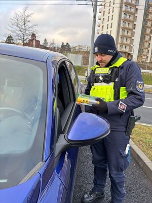 Zdjęcie przedstawiające policjanta, który wręcza kierowcy latarkę samochodową.