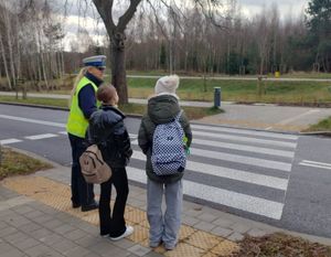 Zdjęcie przedstawiające policjantkę ruchu drogowego, która rozmawia z dwiema dziewczynkami na temat bezpiecznego przechodzenia przez przejście dla pieszych.