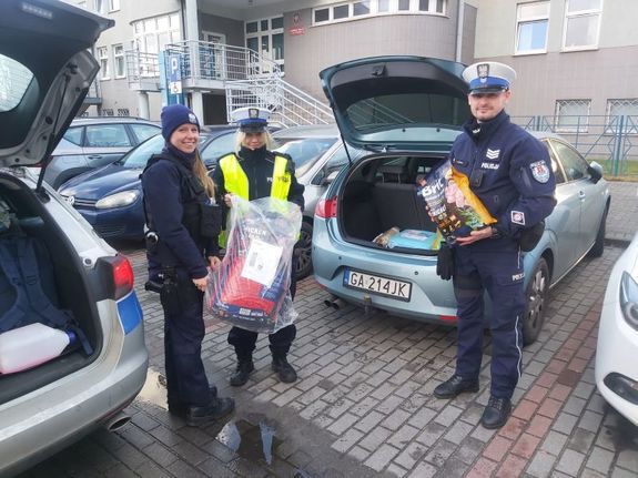 Zdjęcie przedstawiające trzech policjantów i jedną policjantkę z prezentami na tle radiowozów