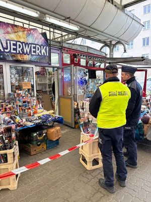 Zdjęcie przedstawiające policjanta i funkcjonariusza Straży Miejskiej podczas kontroli punktu sprzedaży fajerwerków.